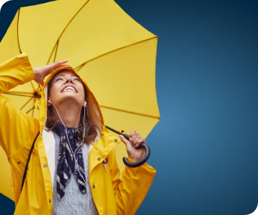 Smiling young woman in yellow raincoat holding yellow umbrella and looking upwards