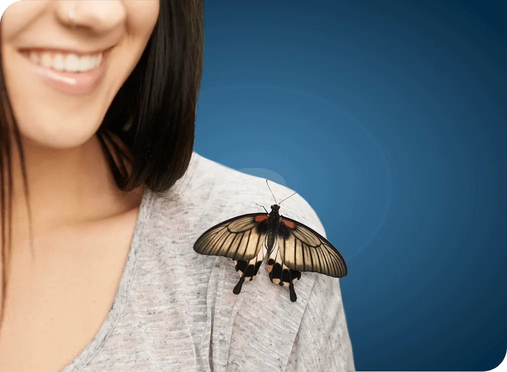 Cropped shot of a grey butterfly perched on a smiling woman’s shoulder